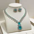 A silver-tone jewelry set displayed on a cream jewelry bust, featuring a necklace and matching earrings with bright turquoise-colored rectangular gemstones and clear pavé accents.