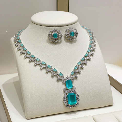 A silver-tone jewelry set displayed on a cream jewelry bust, featuring a necklace and matching earrings with bright turquoise-colored rectangular gemstones and clear pavé accents.