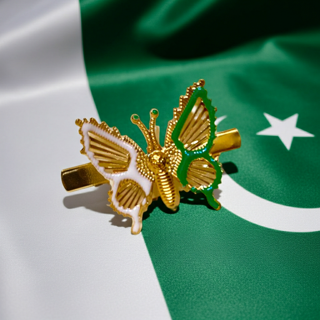 A gold butterfly-shaped hair clip with white and green enamel details, displayed on a green and white Pakistani flag background.