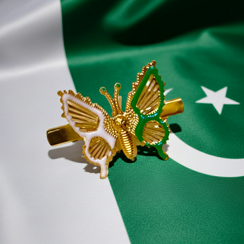 A gold butterfly-shaped hair clip with white and green enamel details, displayed on a green and white Pakistani flag background.