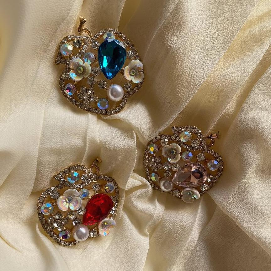 Three ornate brooches with gemstones on a beige fabric background