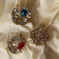 Three ornate brooches with gemstones on a beige fabric background