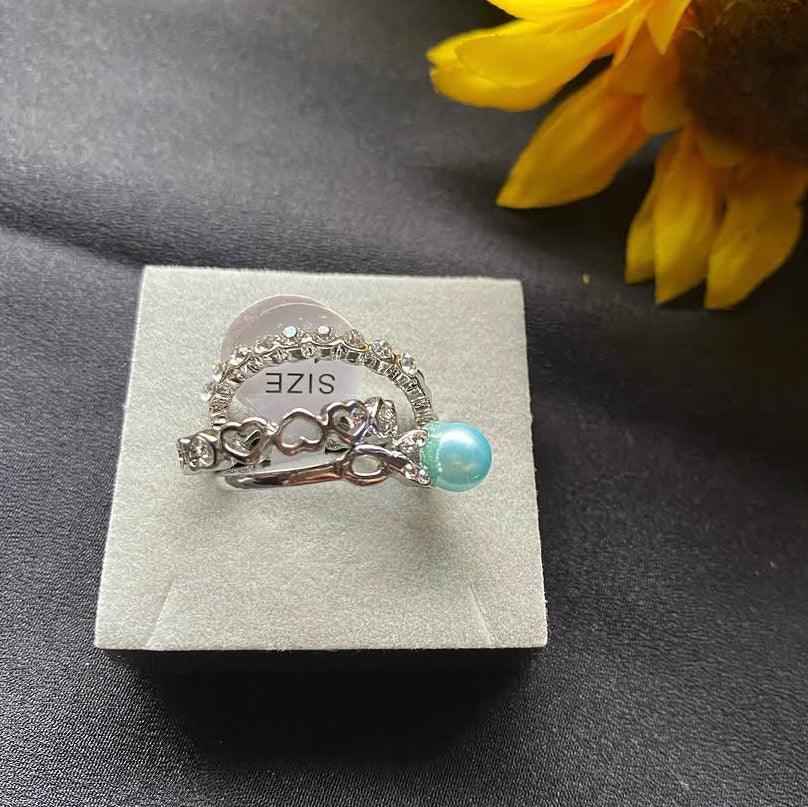 Silver ring with a turquoise bead on a gray display card, next to a yellow flower.