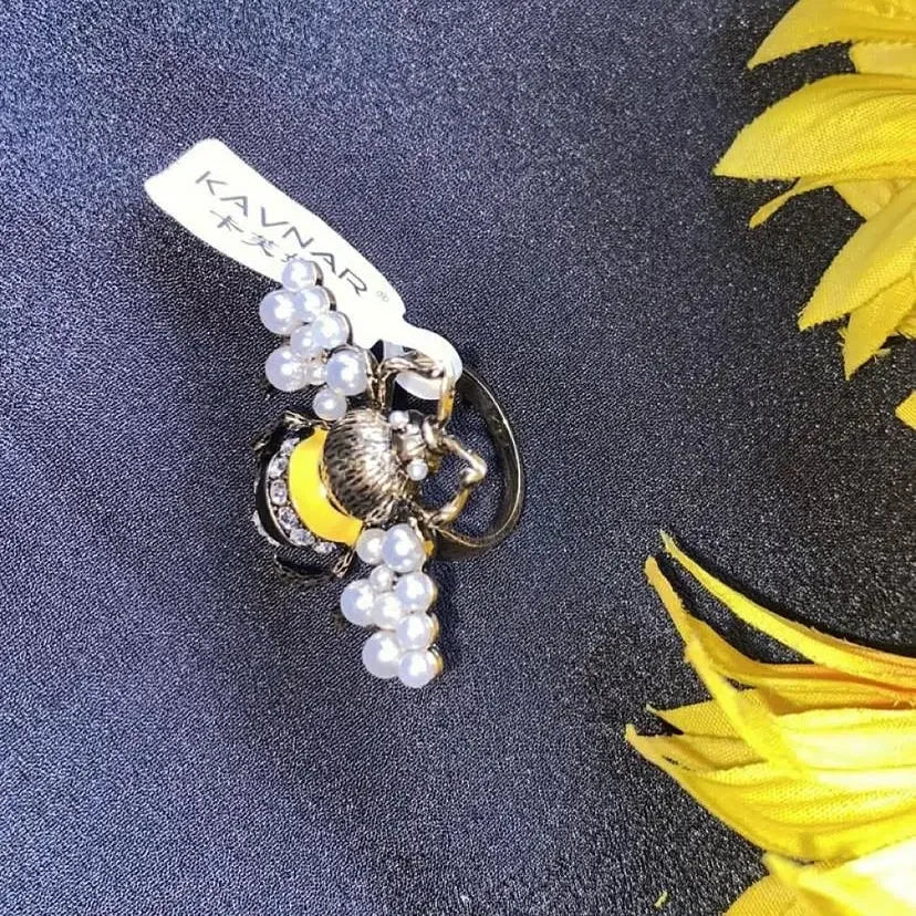 Keychain with grapes and a bee on a dark surface with yellow feathers
