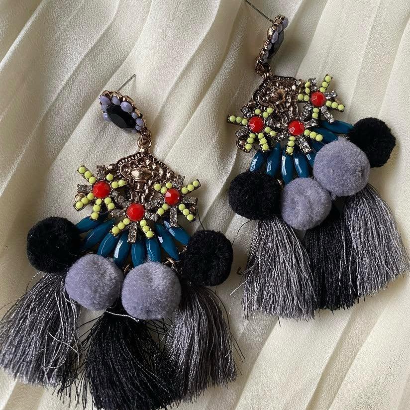 Decorative earrings with tassels and pom-poms on a textured white background