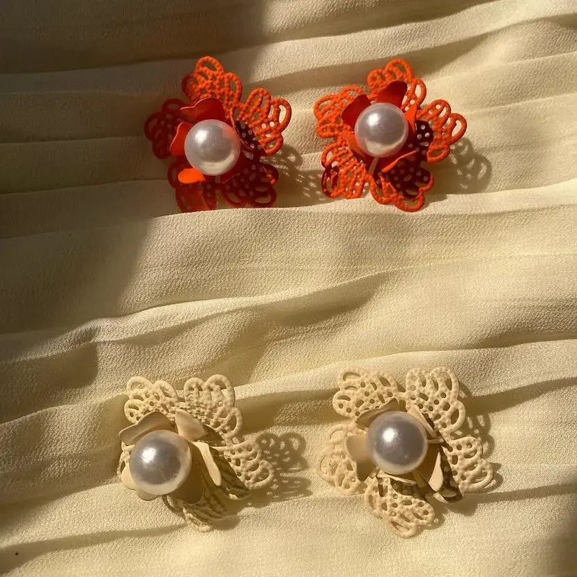 Pair of red floral earrings with pearl centers on a beige fabric background