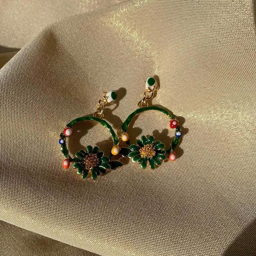 Decorative earrings with green and gold design on a textured beige surface