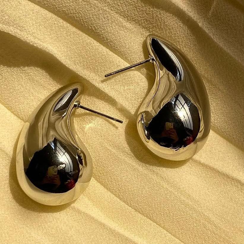 Shiny silver earrings on a beige fabric background