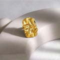 Gold mask-shaped earring on a light beige surface