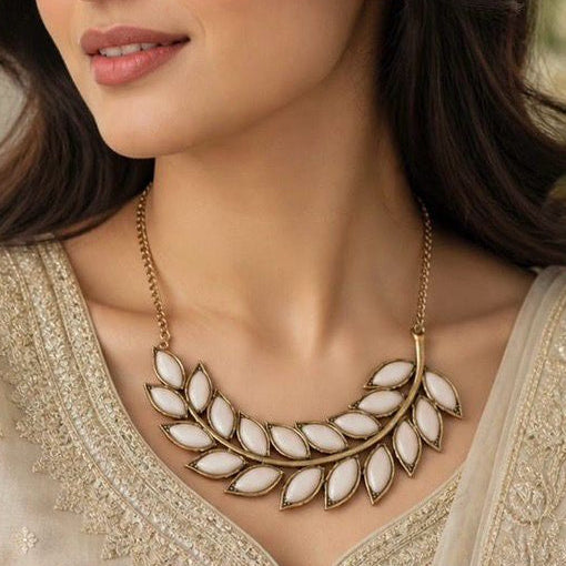Close-up of a woman wearing a gold and white leaf-shaped necklace.