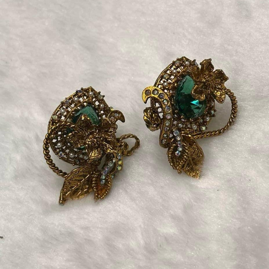 Pair of gold and green earrings on a textured white surface