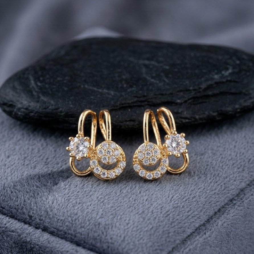 Gold hoop earrings with circular designs and clear stones on a dark fabric background
