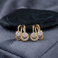 Gold hoop earrings with circular designs and clear stones on a dark fabric background