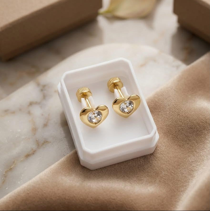 Gold heart-shaped earrings in a box with a marble surface and 'Aurelia' branding.