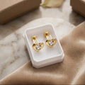 Gold heart-shaped earrings in a box with a marble surface and 'Aurelia' branding.