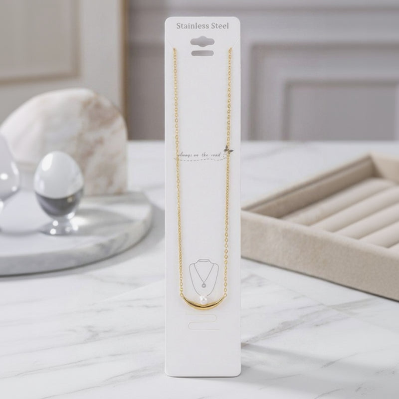 Gold necklace on a white card with 'Stainless Steel' text, placed on a marble surface.