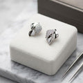 Silver leaf-shaped earrings on a white jewelry cushion with a marble surface.