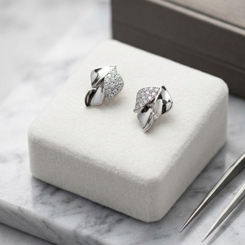 Silver leaf-shaped earrings on a white jewelry cushion with a marble surface.
