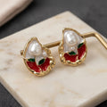Gold earrings with pearls and red stones on a marble surface