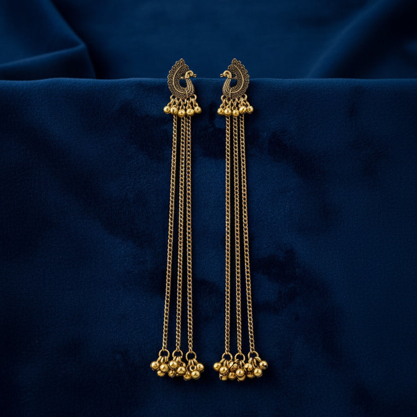 Gold earrings with chain and bead details on a dark blue fabric background
