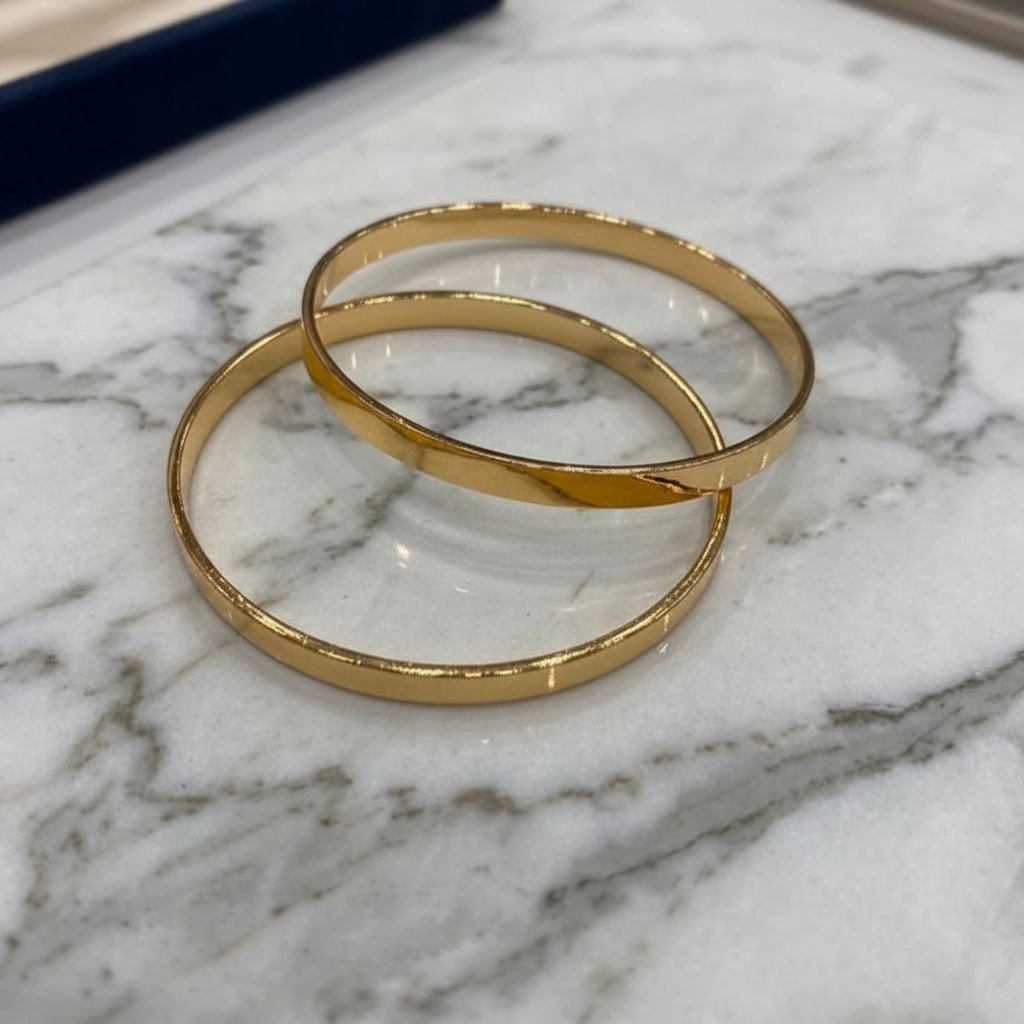 Two gold bangles on a marble surface
