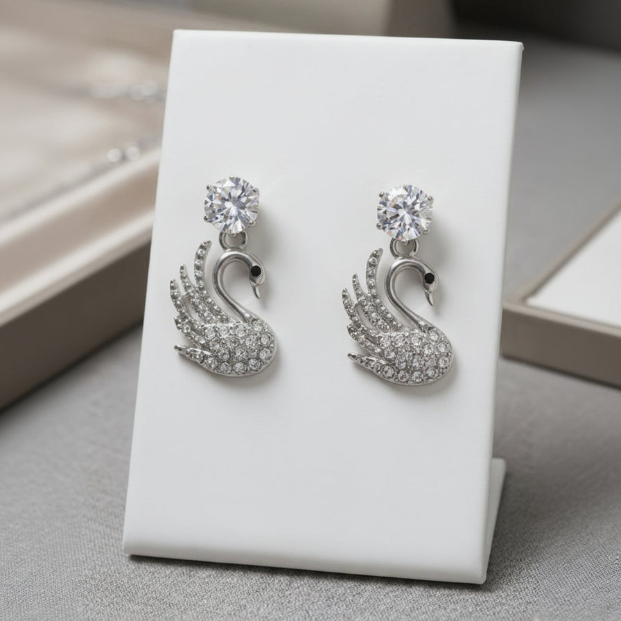 Silver swan-shaped earrings on a white card with a neutral background