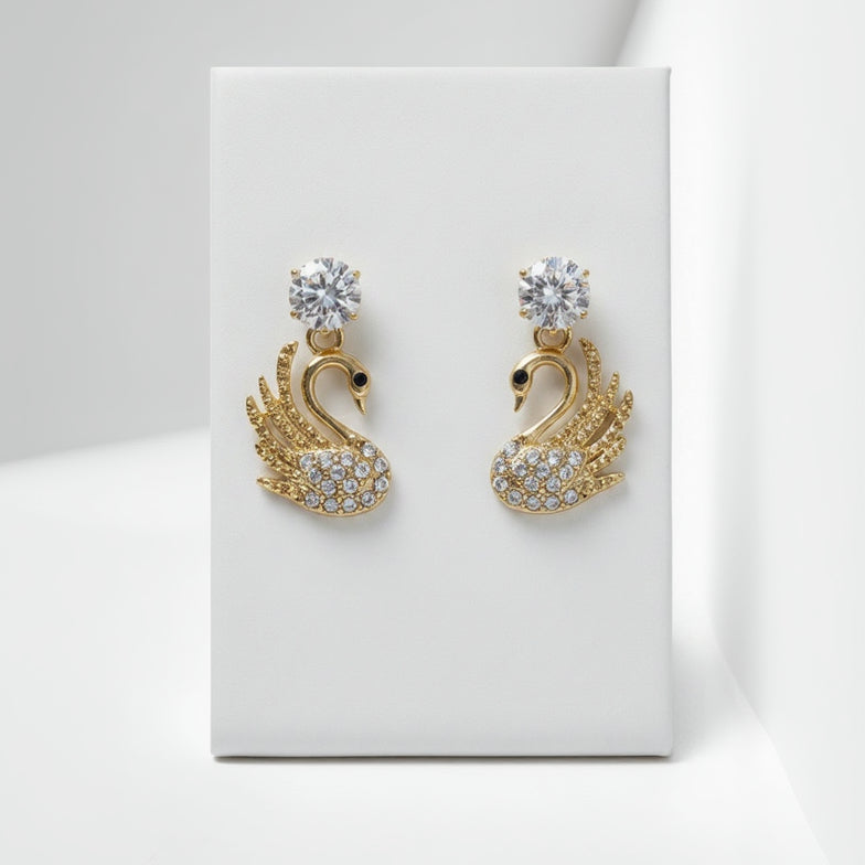 Gold swan-shaped earrings with crystal details on a white card