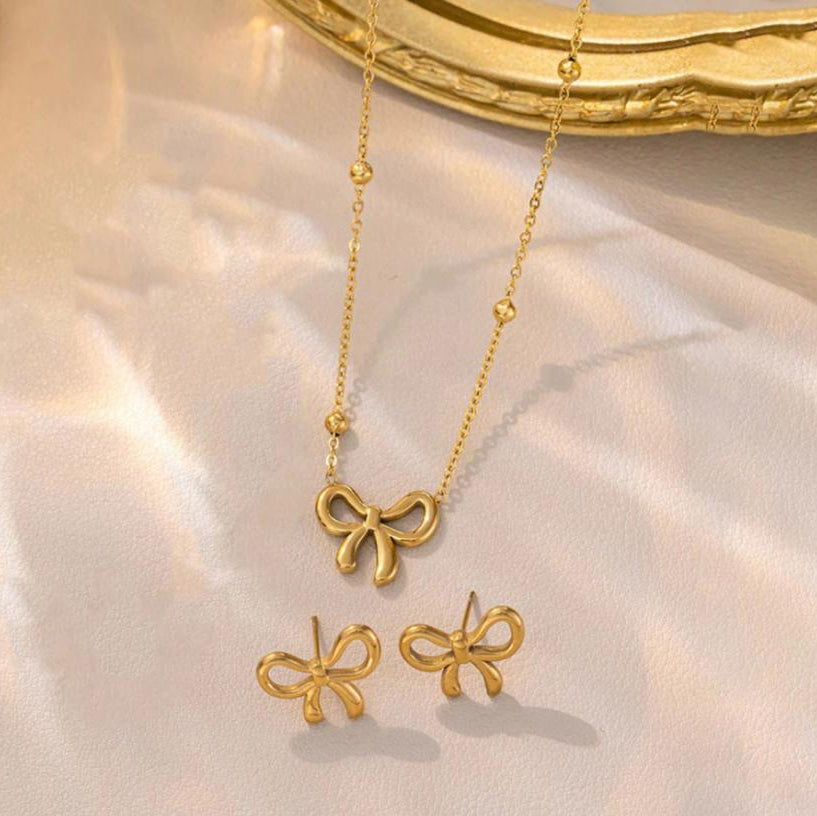 Gold bow-shaped necklace and earrings on a soft fabric background