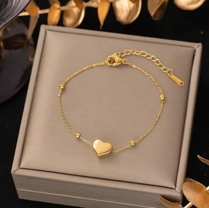 Gold bracelet with a heart charm on a gray jewelry box