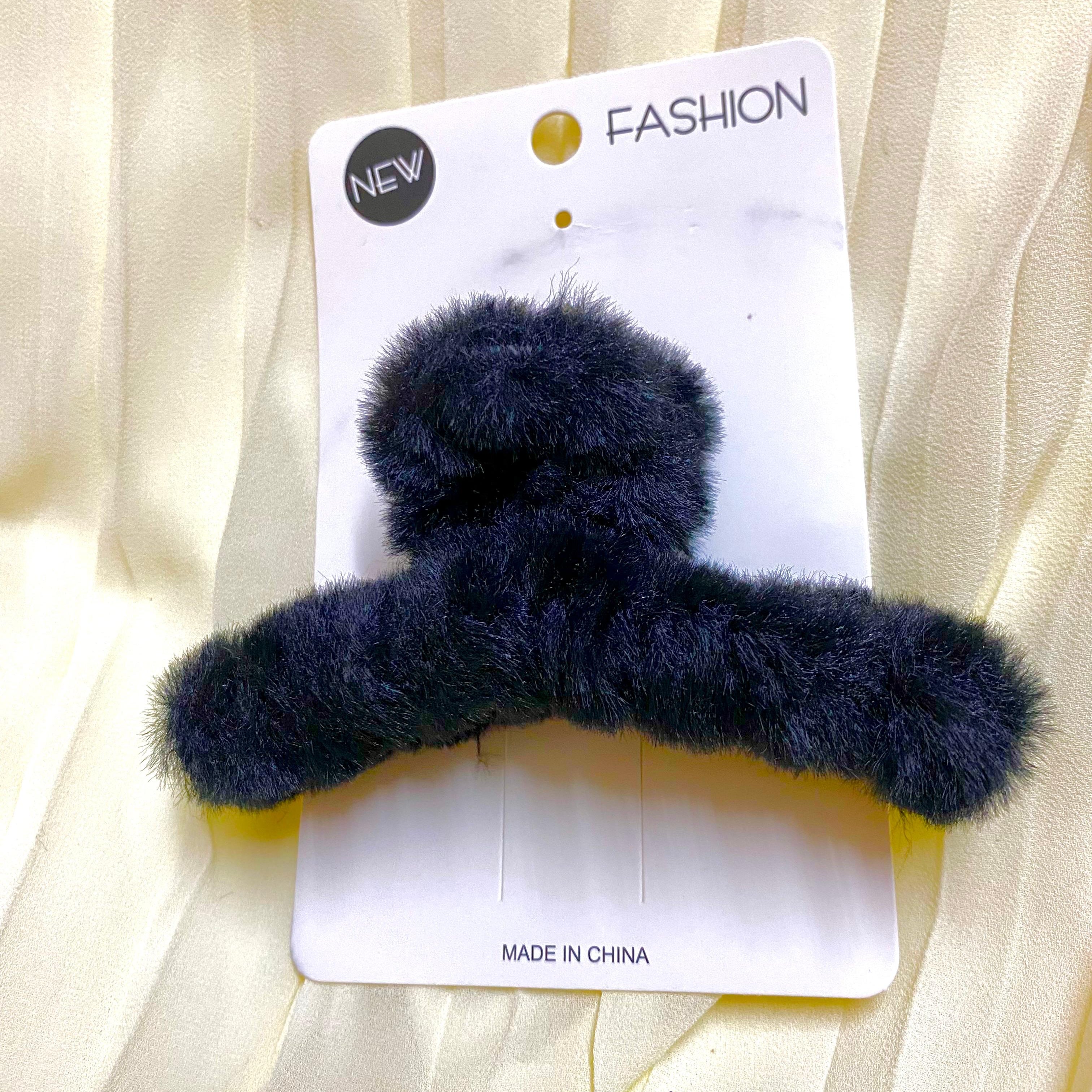 Navy blue fuzzy hair clip on a white card with 'New Fashion' text, against a beige fabric background.
