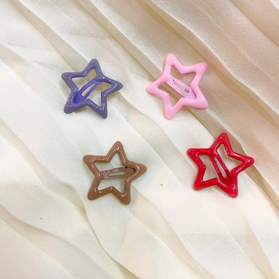 Four star-shaped hair clips in purple, pink, brown, and red on a sheer fabric background.