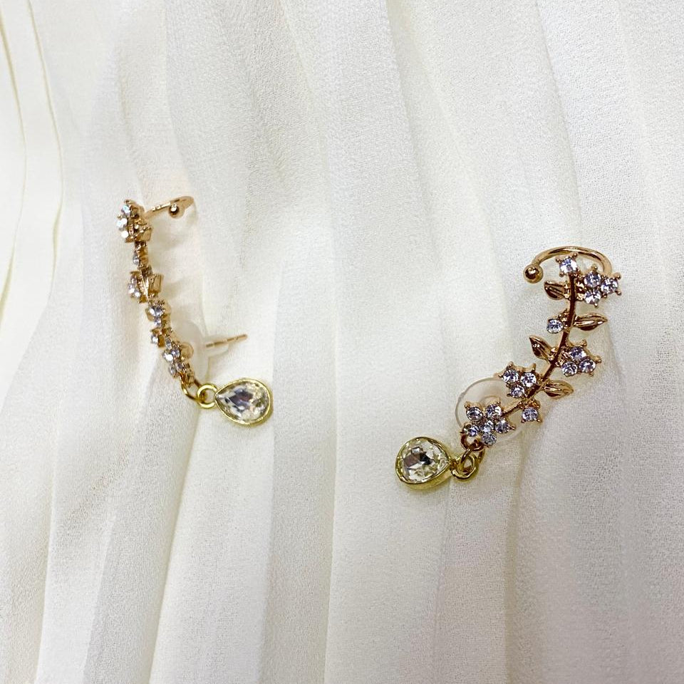 Gold earrings with floral designs on a white fabric background