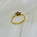 Gold ring with a black flower-shaped design on a textured white surface