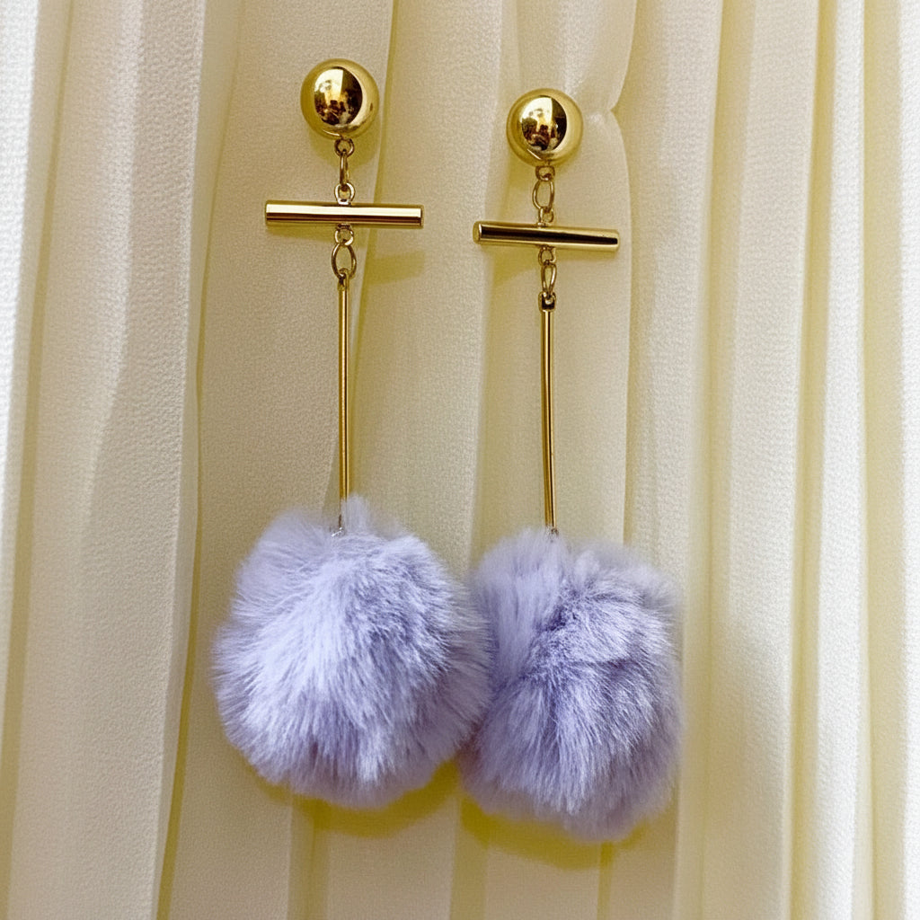 Gold earrings with purple pom-poms on a beige curtain background