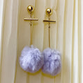 Gold earrings with purple pom-poms on a beige curtain background