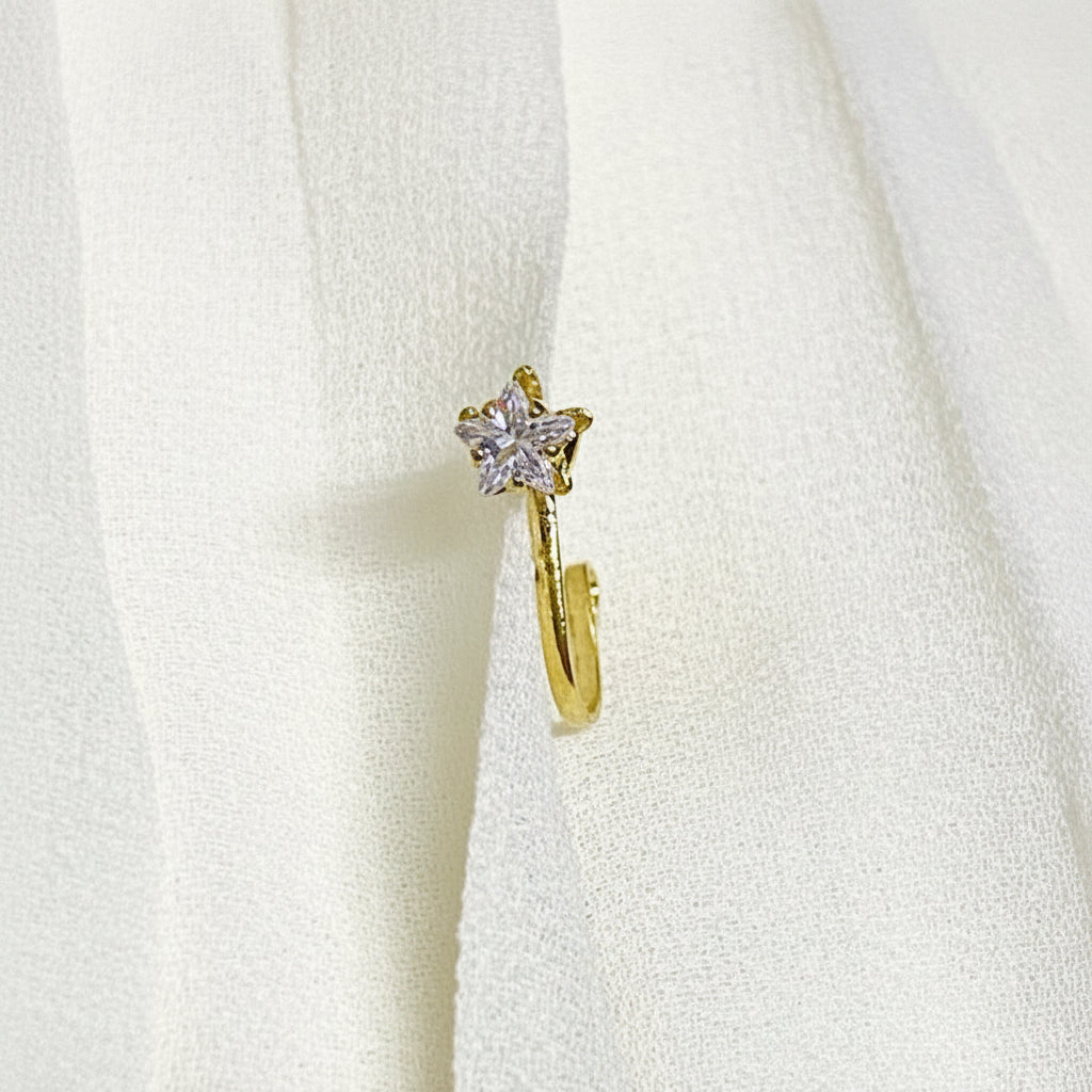 Gold earring with a star-shaped gemstone on a white textured background
