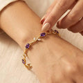 Gold bracelet with purple gemstones on a wrist against a beige background