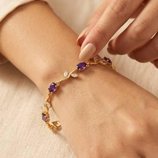 Gold bracelet with purple gemstones on a wrist against a beige background