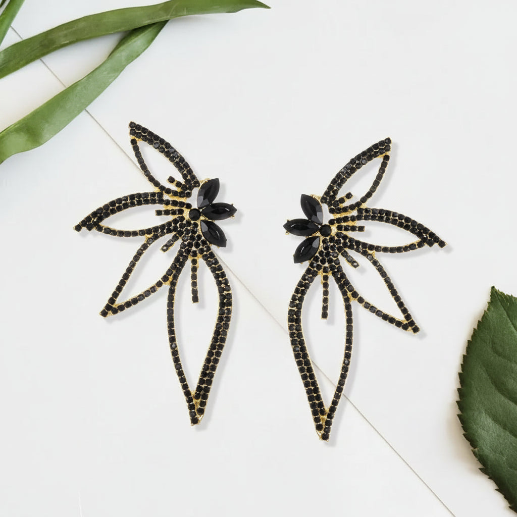 Pair of black and gold earrings on a white surface with green leaves.