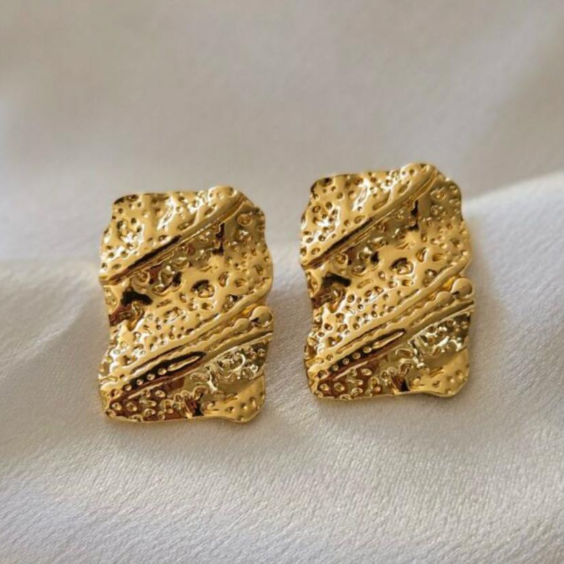 Pair of gold textured square earrings on a white fabric background