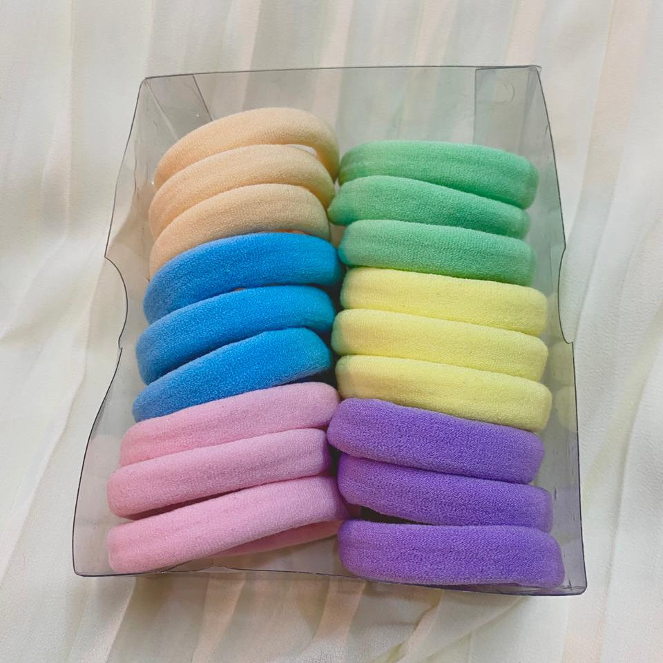 Set of colorful hair elastics in a clear plastic box on a light fabric background