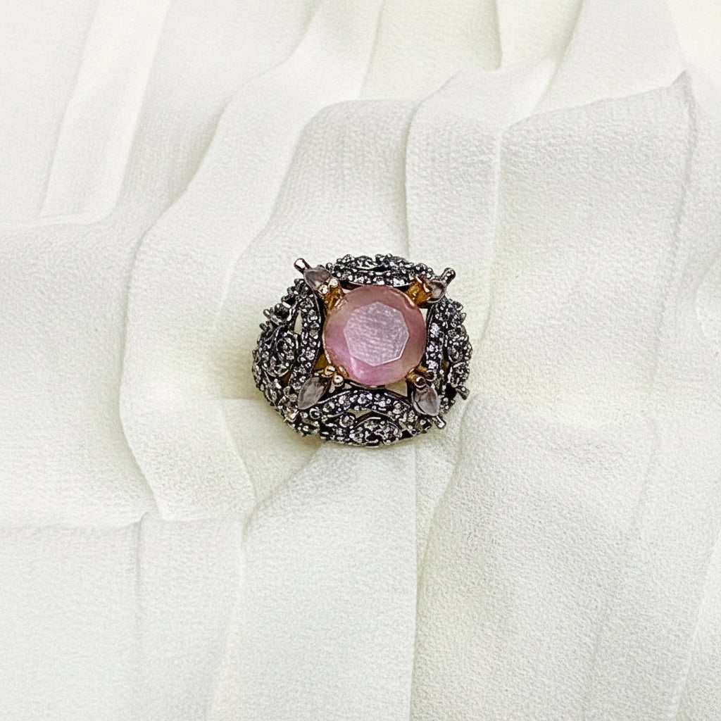 Pink stone brooch with decorative frame on a white fabric background