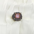 Pink stone brooch with decorative frame on a white fabric background