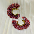Pair of earrings with red and gold design on a white fabric background