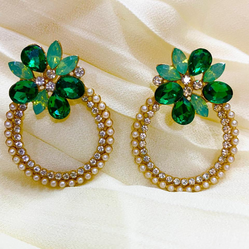 Pair of earrings with green gemstones and pearl-like beads on a beige fabric background