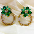 Pair of earrings with green gemstones and pearl-like beads on a beige fabric background