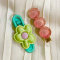 Green and pink flower-shaped hair clip on a white fabric background