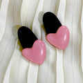 Pair of pink and black heart-shaped earrings on a white fabric background