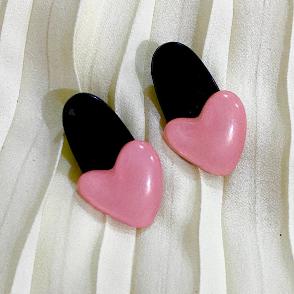 Pair of pink and black heart-shaped earrings on a white fabric background