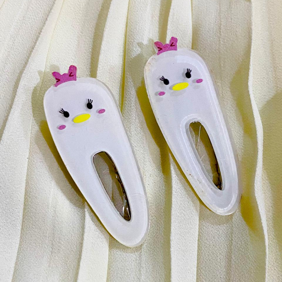 Two white hair clips with cartoon face design on a beige fabric background